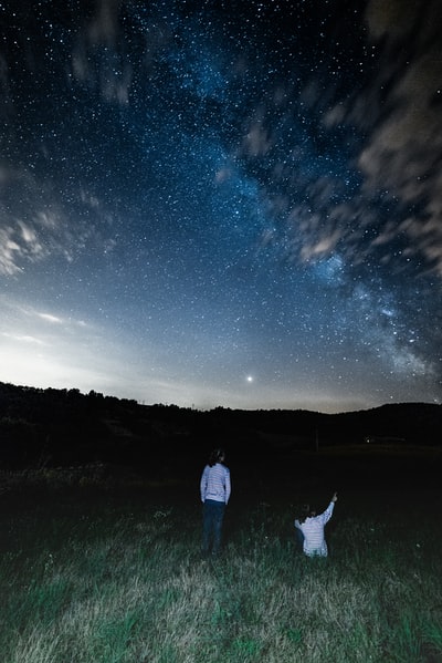 两个穿着白衬衫的人在田野里观看夜空中的星星编队